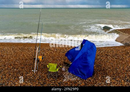 Ein Fischer versucht, sein Zelt an EINEM windigen Tag am Hove Beach, Hove, East Sussex, Großbritannien, einzurichten. Stockfoto