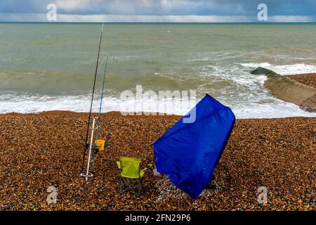 Ein Fischer versucht, sein Zelt an EINEM windigen Tag am Hove Beach, Hove, East Sussex, Großbritannien, einzurichten. Stockfoto