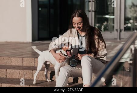 Attraktive junge Frau mit Hund sitzt auf der Treppe. Parson russell Terrier gähnt Stockfoto