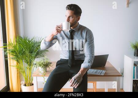 Hübscher Mann in einem Hemd, der in seinem Büro Kaffee trinkt Stockfoto