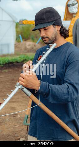 Junger Mann Bauer, Gärtner, Porträt mit seinem Rechen bereitet ihn für die Arbeit in Pflanzen, Gemüse. Stockfoto