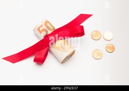 Rolle von Euro-Banknoten, umgeben von einem roten Band und einer hübschen Schleife. Buntes Band um Euro-Banknoten. Verschenken Sie Geld. An zu spenden Stockfoto