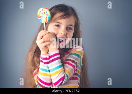 Kleines Kind, das Lutscher isst. Happy schönes Mädchen mit Süßigkeiten isoliert auf blauem Hintergrund. Stockfoto