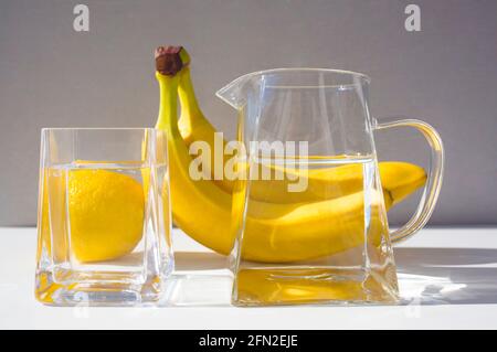 Reines Wasser in Glaskrug und Glas, gelbe Früchte auf dem Hintergrund. Stockfoto