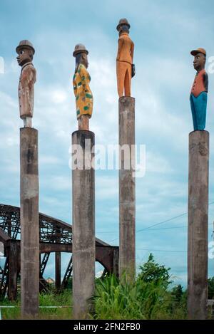 Vier Holzstatuen mit Hüten auf Stöcken im alten Sanaga River Bridge Stockfoto