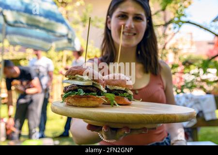 Nahaufnahme mit selektivem Fokus von einer jungen Frau, die ein hölzerner Servierbrett mit köstlichen Burgern hält. Stockfoto