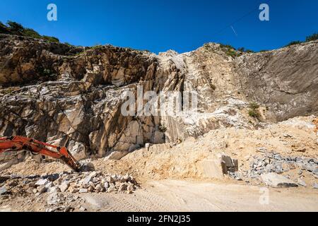 Orange Raupenbagger in einem Steinbruch aus weißem Marmor. Apuanische Alpen (Alpi Apuane), Provinz Massa und Carrara, Toskana, Italien, Europa. Stockfoto