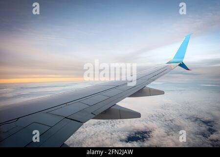 Verkehrsflugzeug, während Sie bei Sonnenuntergang über den Wolken fliegen. Blick durch das Flugzeugfenster. Stockfoto