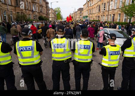 Glasgow, Schottland, Großbritannien. Mai 2021. Demonstranten versammeln sich in Pollokshields, um die Abschiebung von Einzelpersonen aus dem Haushalt zu verhindern. Die starke Polizeipräsenz setzt sich fort, wobei die Polizei und die Demonstranten, die in der Kenmure Street Street sitzen und den Zugang blockieren, angespannt sind. Kredit: Iain Masterton/Alamy Live Nachrichten Stockfoto