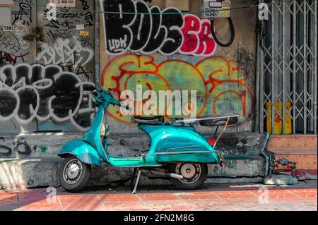 Chinatown, Bangkok – 20,2021. März: Der alte Roller wurde unbeaufsichtigt auf dem Bürgersteig vor einer alten Mauer mit Graffiti auf der ganzen Straße gelassen. Stockfoto