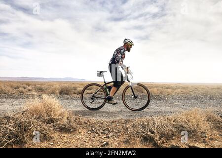 Fahrer mit Bart fährt bei sonnigem Wetter in Kasachstan mit dem Mountainbike auf der Wüstenstraße. Konzept für Extremsport und Outdoor-Erholung. Stockfoto