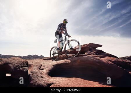 Reiter mit Bart fährt sein Mountainbike im Wüstenvulkanischen Berg im Nationalpark Altyn Emel in Kasachstan. Extremsport und Outdoor recreati Stockfoto