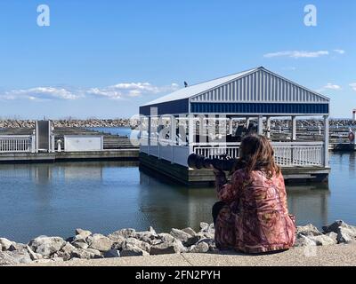 DER FOTOGRAF SITZT AM PIER UND FOTOGRAFIERT VÖGEL MIT LANGER LINSE WÄHREND DER COVID-19-PANDEMIE. Stockfoto