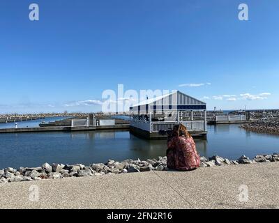 DER FOTOGRAF SITZT AM PIER UND FOTOGRAFIERT VÖGEL MIT LANGER LINSE WÄHREND DER COVID-19-PANDEMIE. Stockfoto