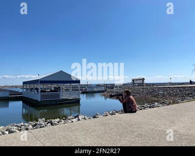 DER FOTOGRAF SITZT AM PIER UND FOTOGRAFIERT VÖGEL MIT LANGER LINSE WÄHREND DER COVID-19-PANDEMIE. Stockfoto