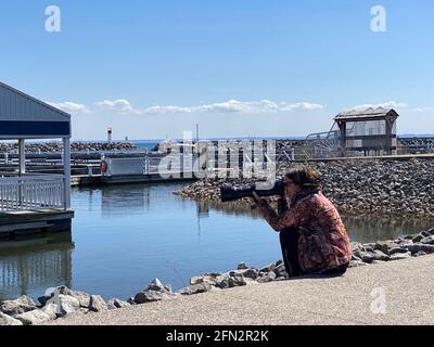 DER FOTOGRAF SITZT AM PIER UND FOTOGRAFIERT VÖGEL MIT LANGER LINSE WÄHREND DER COVID-19-PANDEMIE. Stockfoto