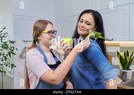 Freundliche fröhliche Familie, Porträt von Mutter und Tochter im Teenageralter, mit grünem Papagei Stockfoto