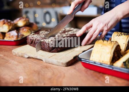 Verkaufsassistent In Bäckerei Schneiden Frisch Gebackene Brownies Auf Zähler Stockfoto