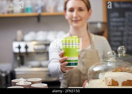 Weibliche Mitarbeiterin im Café serviert Kaffee in einer nachhaltigen wiederverwendbaren Tasse Stockfoto