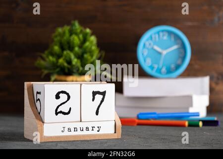 Januar. Januar 27 Holzwürfelkalender mit unscharfen Objekten auf dem Hintergrund. Stockfoto