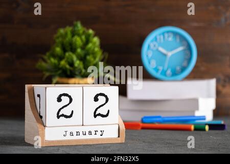 Januar. Januar 22 Holzwürfelkalender mit unscharfen Objekten auf dem Hintergrund. Stockfoto