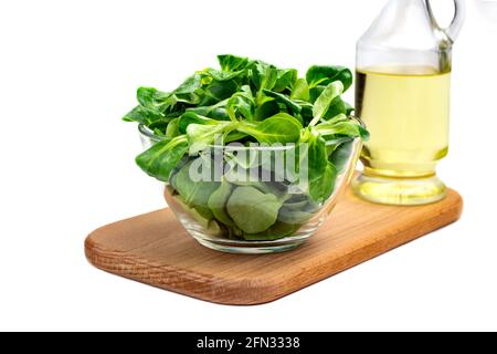 Mungbohnensalatblätter, Maissalat in einer Glasschüssel auf einem Holzbrett, isolieren. Frische Mischung aus grün gewaschenen Blättern und Pflanzenöl (Valerianella locu Stockfoto