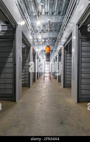 Der Elektriker des Bauarbeiters verdrahtet die Lichter an der Leiter im Gebäude im Bau. Stockfoto