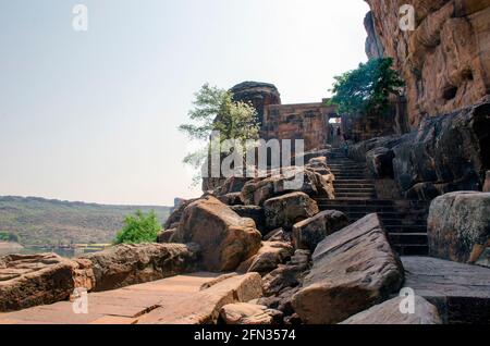 Bilder von der Straße und der Treppe zum Badami Cave Temple. Ein Baum am Straßenrand ist in der fernen Landschaft mit ihm zu sehen. Stockfoto