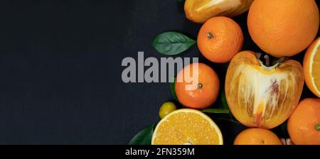 Orangefarbene Früchte mit Blättern auf schwarzem Hintergrund. Draufsicht. Stockfoto