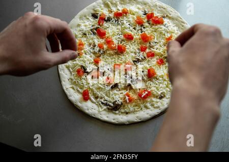 Pizzaiolo, der Koch bereitet hausgemachte leckere Pizza mit Pilzen in der Küche. Draufsicht. Hände aus der Nähe gießen Tomate Stockfoto