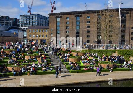 Die Menschen genießen die Sonne auf den Stufen am Granary Square in King's Cross. Stockfoto