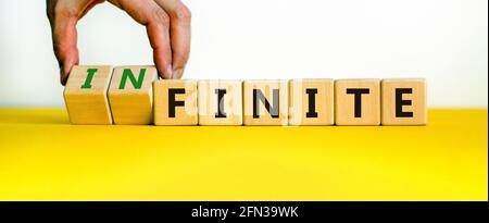 Endliches oder unendliches Symbol. Geschäftsmann dreht Holzwürfel und ändert das Wort 'endlich' in 'unendlich'. Schöner gelber Tisch, weißer Hintergrund. Busin Stockfoto