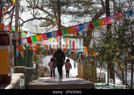 Frau von hinten gesehen, die mit ihren beiden Kindern inmitten der Gebetsfahnen spazierend ist.Shangri La, Yunan. Volksrepublik China 2019 Stockfoto