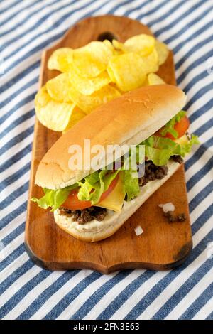 Hausgemachtes, gehacktes Rindfleisch-Sandwich mit Kartoffelchips auf einem rustikalen Holzbrett, Seitenansicht. Stockfoto