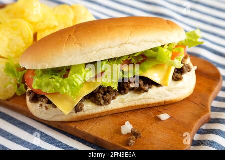 Hausgemachtes, gehacktes Rindfleisch-Sandwich mit Kartoffelchips auf einem rustikalen Holzbrett, Seitenansicht. Stockfoto