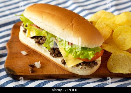 Hausgemachtes, gehacktes Rindfleisch-Sandwich mit Kartoffelchips auf einem rustikalen Holzbrett, Seitenansicht. Stockfoto