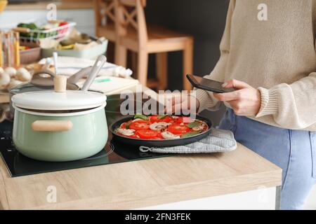 Junge Frau fotografiert leckere Pizza in der Küche Stockfoto