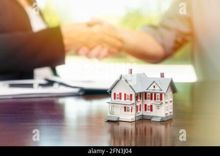 Immobilienmakler und Kunde unterzeichnen Vertragsdokumente und schütteln sich die Hände mit kleinen Modell Haus vor. Stockfoto