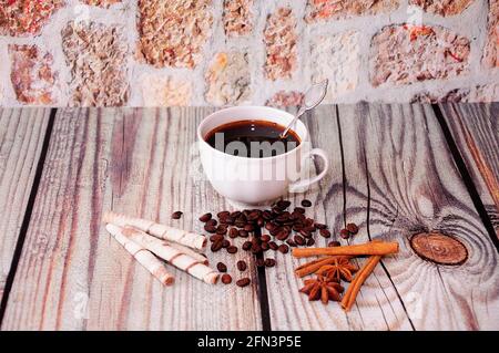 Eine Tasse Kaffee, Waffelrollen, Zimt, Anisbrot und eine Streuung von gerösteten Kaffeebohnen auf einem Holztisch. Nahaufnahme. Stockfoto