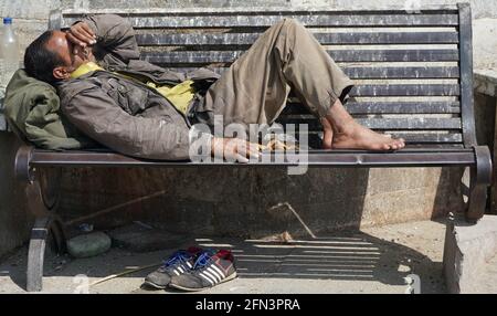 Armer obdachloser Bettler oder Flüchtling, der tagsüber auf einer schmutzigen Holzbank in einer Einbahnstraße in der Stadt schläft. Sozialdokumentarisches Konzept. Schuh Stockfoto