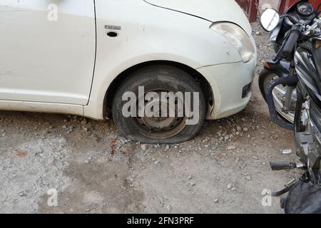 Reifenleck, Nahrad des alten weißen Oldtimers. Autorad: Flacher Reifen auf der Straße. Den Reifen eines alten Autos neben einem Motorrad ablassen. - Udaipur I. Stockfoto