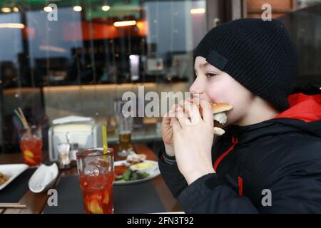 Junge, die im Frühling auf der Restaurantterrasse Burger essen Stockfoto