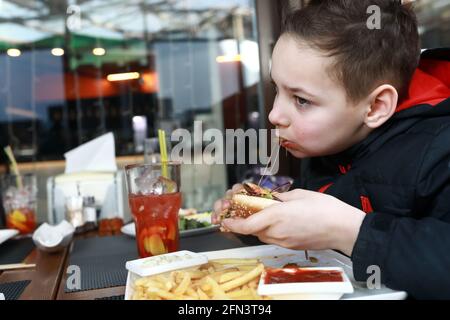 Im Frühling gibt es auf der Restaurantterrasse einen Burger, der von einem Kind beißt Stockfoto