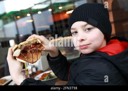 Das Kind hat im Frühling Burger auf der Restaurantterrasse Stockfoto