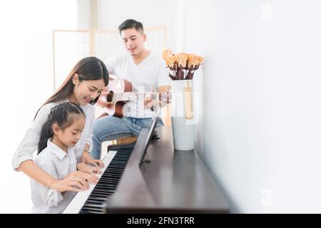 Asiatische Familie, Mutter und Tochter spielen Klavier, Vater spielen Gitarre in Familienband zu Hause, Konzept für Familienbeziehung Stockfoto