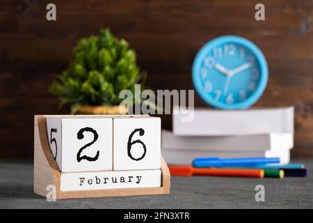 Februar. Februar 26 Holzwürfelkalender mit unscharfen Objekten auf dem Hintergrund. Stockfoto