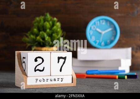 Februar. Februar 27 Holzwürfelkalender mit unscharfen Objekten auf dem Hintergrund. Stockfoto