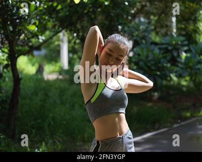Kurzer Schuss einer jungen asiatischen Frau, die ihre Arme streckt Vor dem Training im Park Stockfoto
