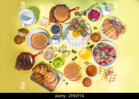 Verschiedene traditionelle Frühstücksgerichte - Spiegeleier mit Speck, Müsli, Hafer, Waffeln, Pfannkuchen, burger, Croissants, Obstbeeren, Kaffee, Tee und Orange j Stockfoto