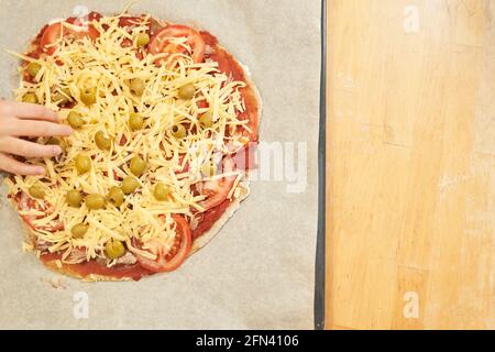 Childs Hand mit Pizza auf Backpapier zum Backen vorbereitet. Gesunde glutenfreie Pizza. Glutenfreier Kochkurs. Foto mit Kopierbereich. Stockfoto